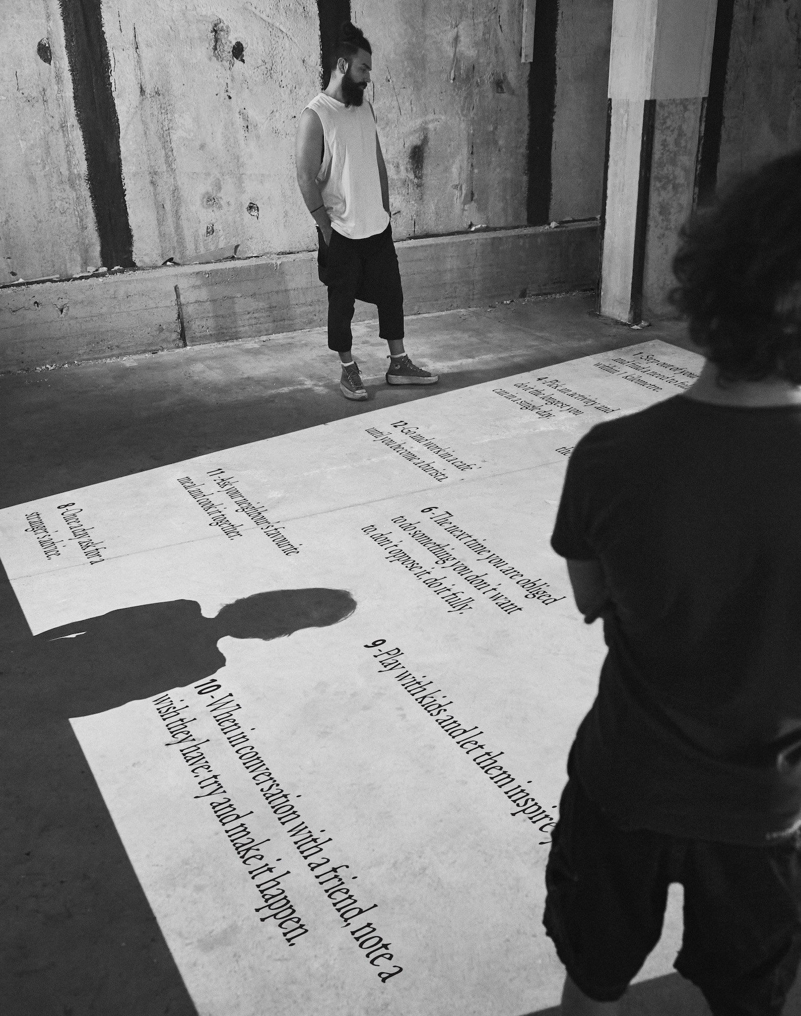 Black and white photo of two people looking at a projection on the floor listing the guidelines of the project.